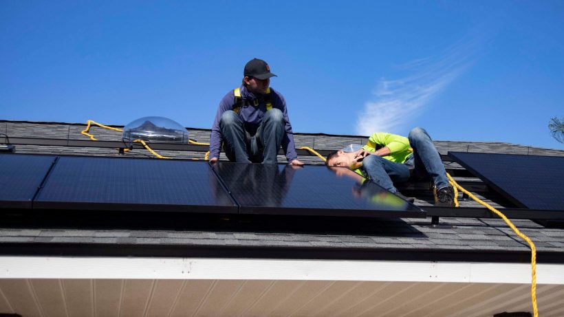 Two workers installing solar panels on roof.