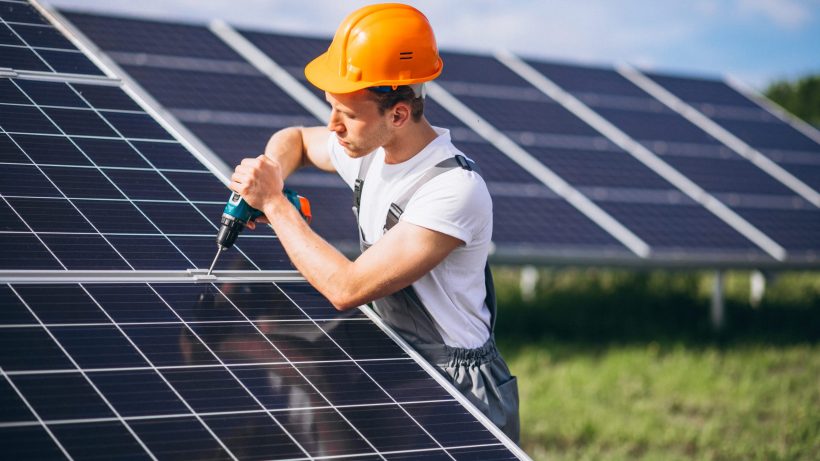 Worker installing solar panel with drill.